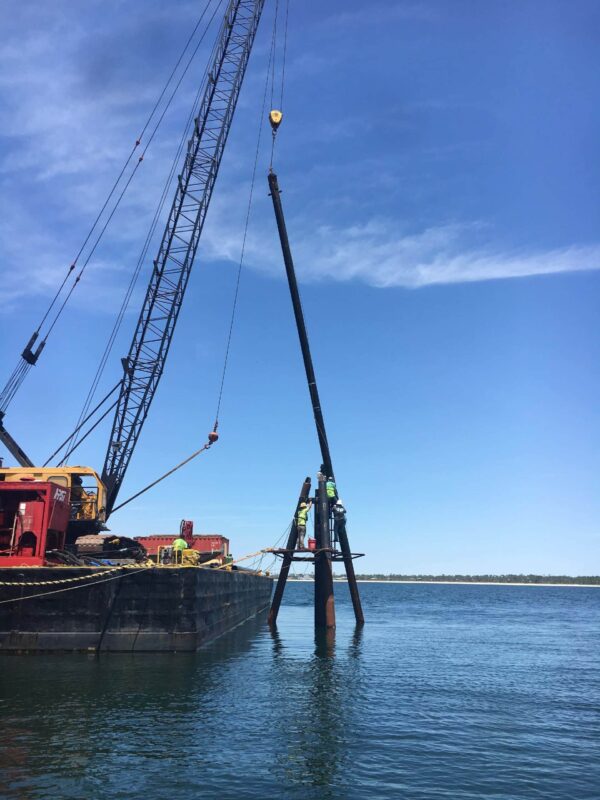 Marine construction project in progress , pole being installed in water with equipment in tow | Inland Construction & Engineering, Inc. Panama City, Florida providing construction, general contracting, marine construction, design & engineering, diving services, roofing, & bulding rehab.